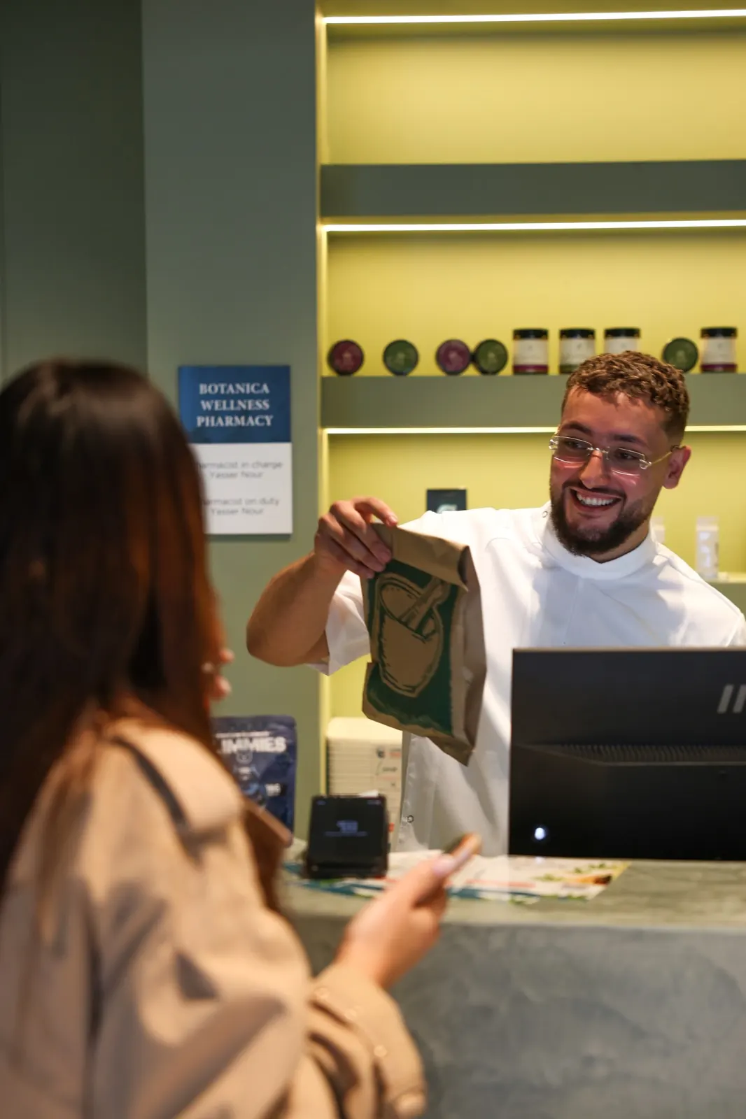 A Botanica pharmacist handing a customer their order at the counter